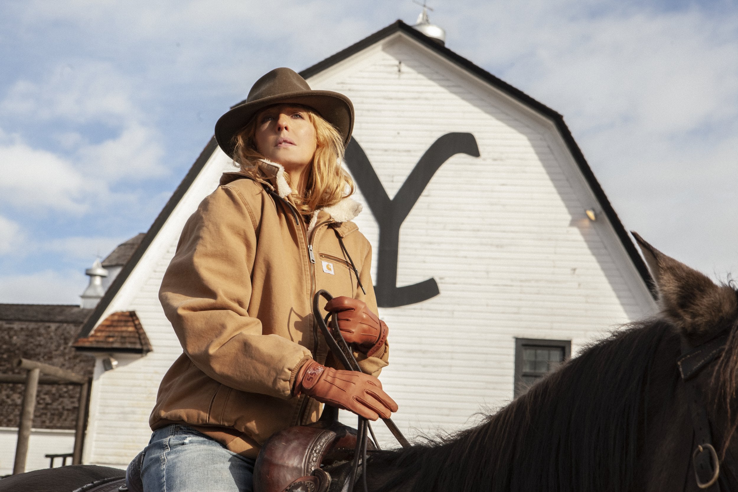 Person on horseback in front of a white building  beth dutton hoodie jacket