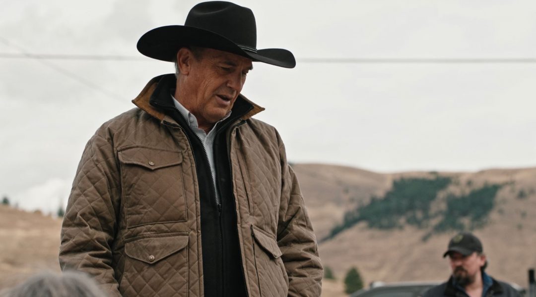 Man wearing a cowboy hat and quilted jacket in a rural setting