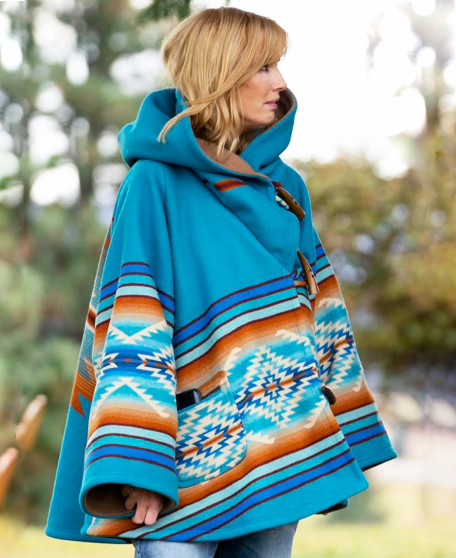Beth Dutton Iconic Blue Coat wearing a blue patterned poncho outdoors with blurred greenery in the background