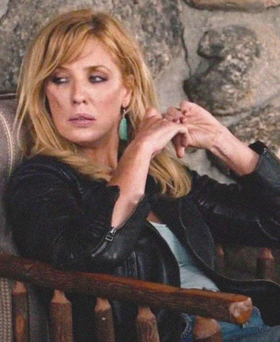 Beth Dutton wear a black leather jacket sitting in a chair.