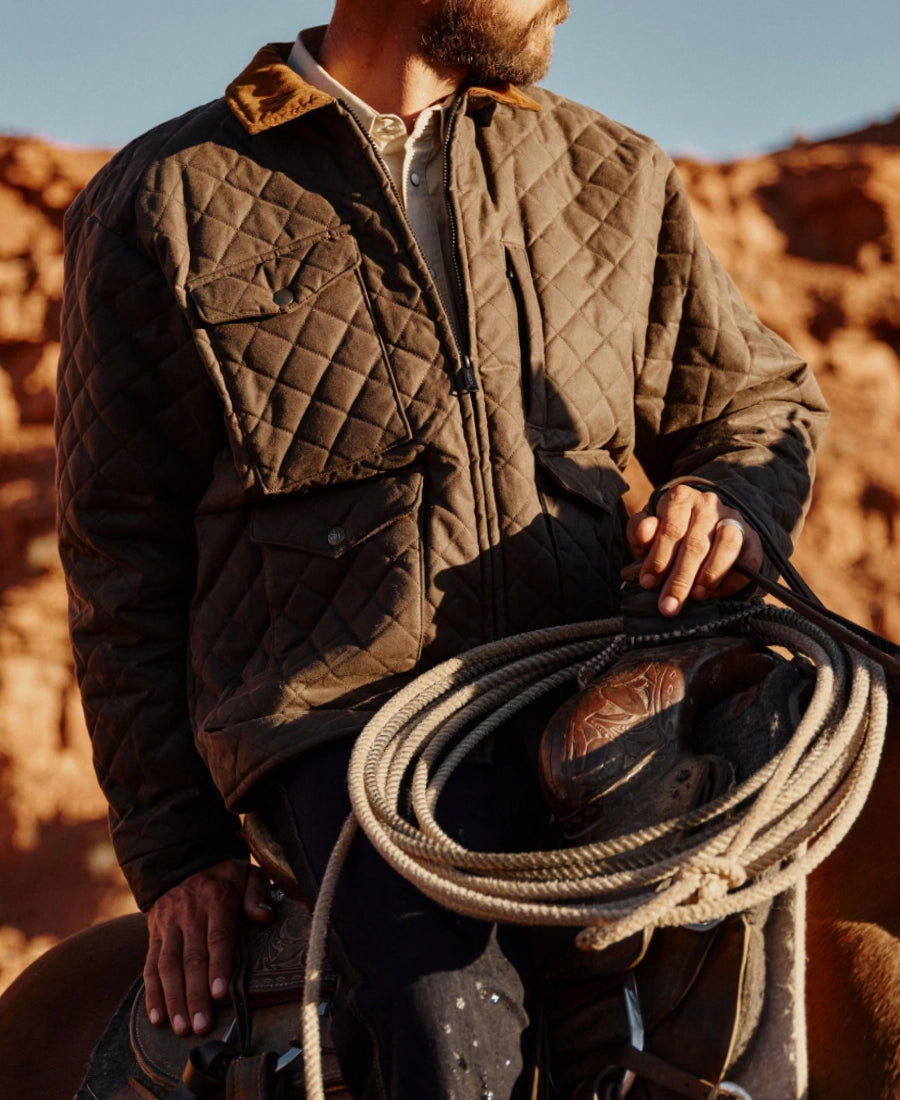 John Dutton Brown Quilted Jacket Yellowstone holding a lasso in a desert setting