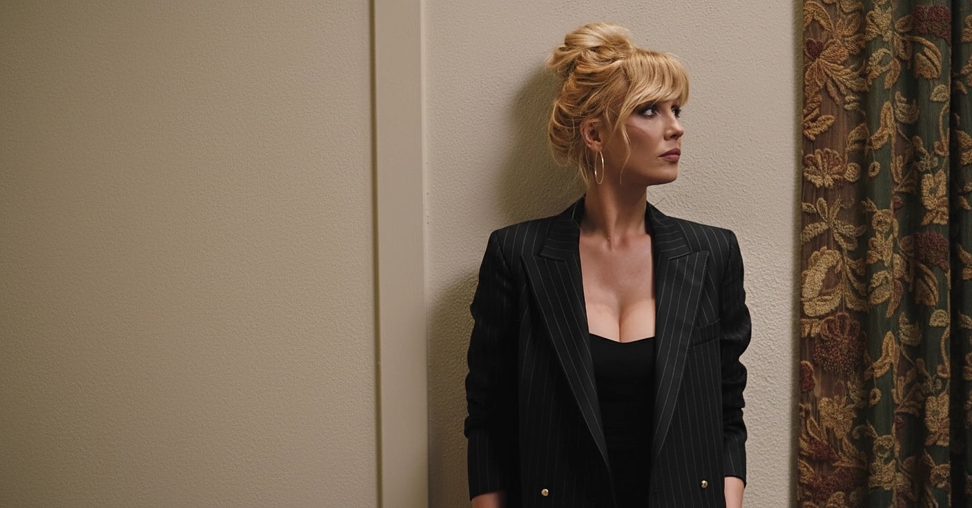 Beth Dutton in a black Striped Blazer standing against a beige wall with a patterned curtain in Yellowstone TV Series