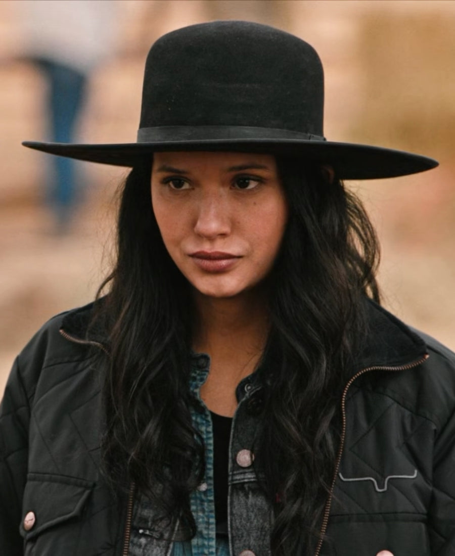 Yellowstone Avery wearing a black wide-brimmed hat and dark jacket with a blurred background