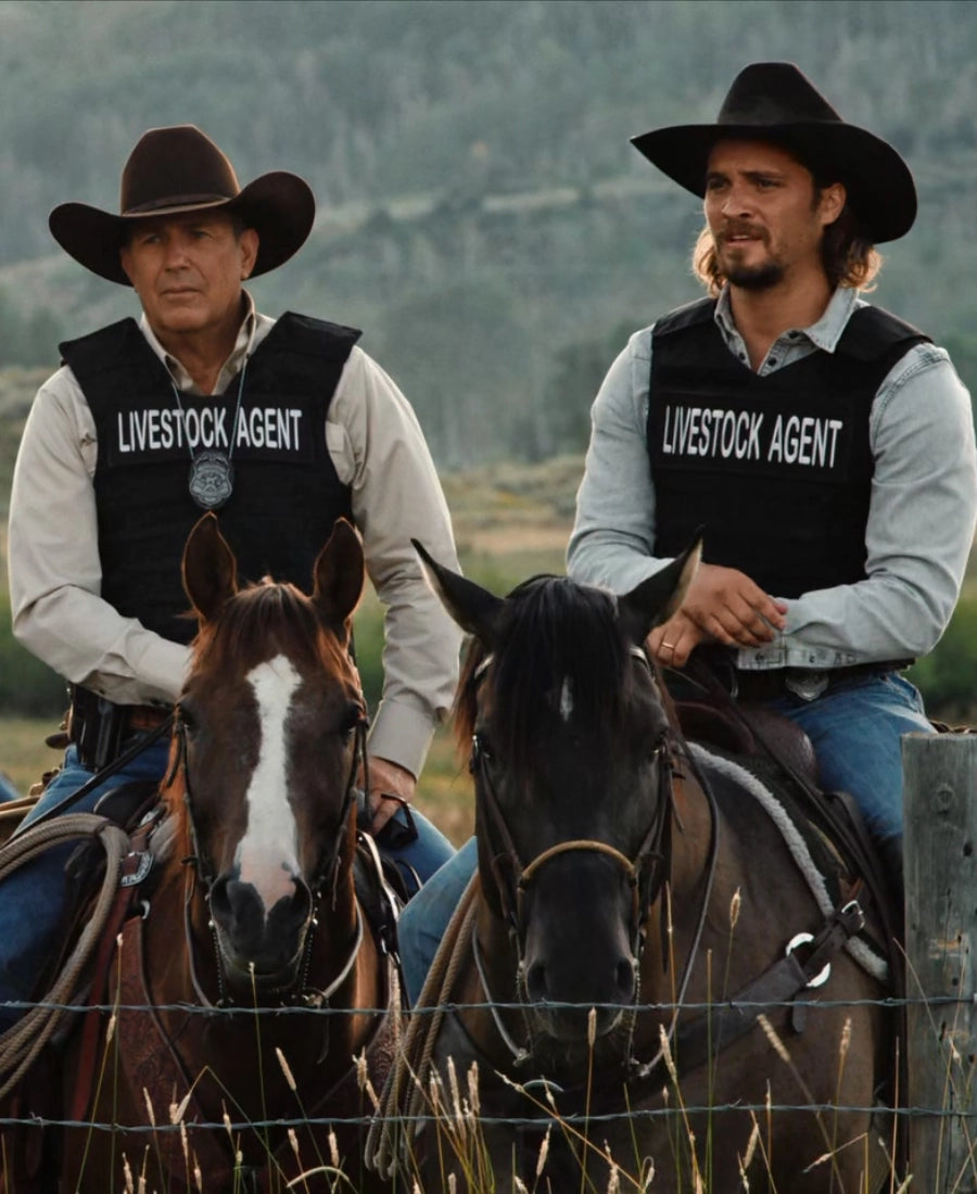 Yellowstone TV Series Two men in livestock agent vests sitting on horses in a field.