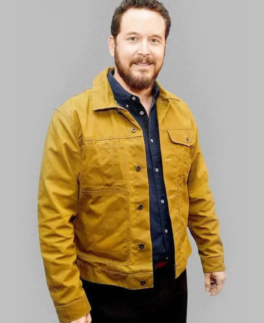 Rip Wheeler wearing a mustard yellow jacket over a dark shirt on a gray background