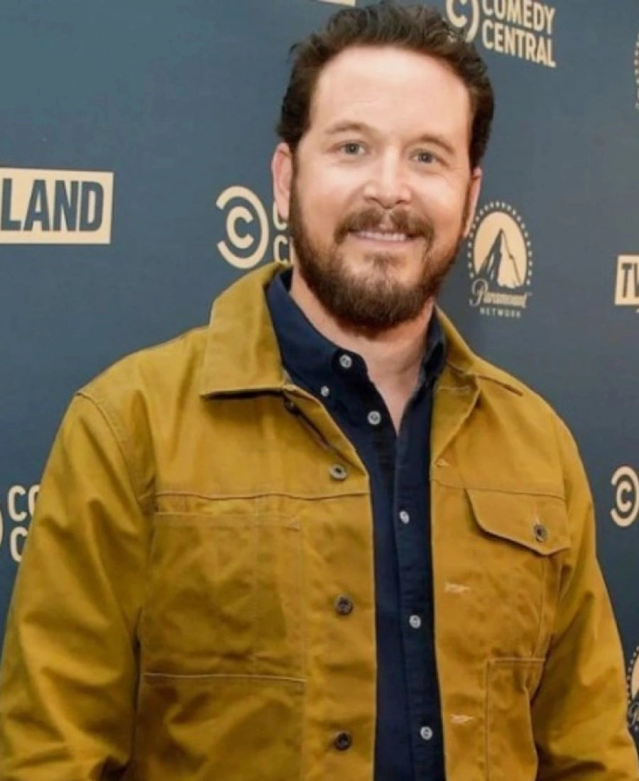 Rip wearing a mustard yellow jacket in front of a blue backdrop with multiple logos.