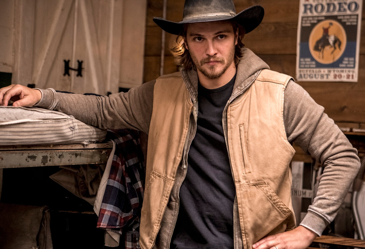 Man in cowboy hat and vest standing in a rustic setting with a 'Rodeo' poster kayce dutton from Yellowstone 