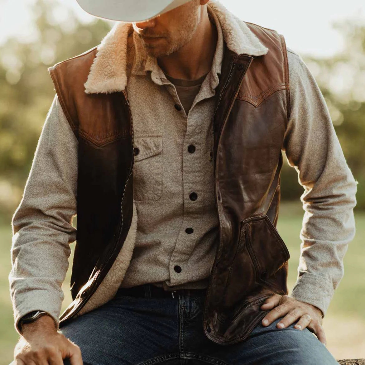 Man wearing a brown leather vest over a beige shirt with a blurred natural background