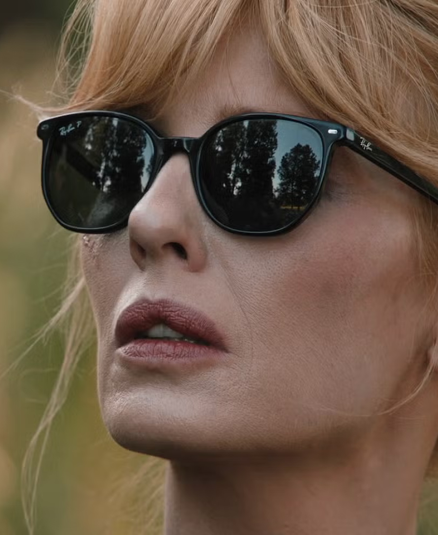 Close-up of a Beth Dutton wearing black sunglasses with a blurred natural background