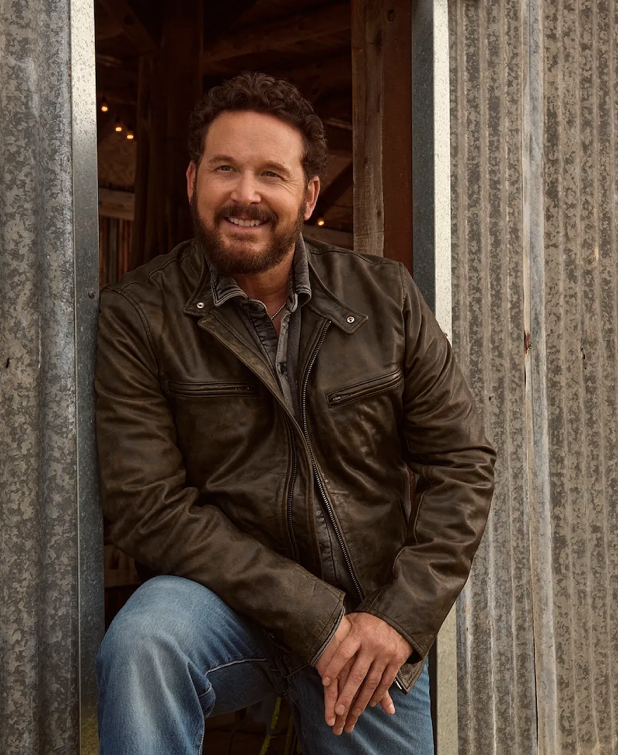 Rip Wheeler Cafe Racer Leather Jacket and blue jeans sitting against a rustic wooden wall.