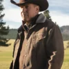john Dutton Yellowstone wearing a brown cowboy hat and jacket in a natural setting with trees and mountains.