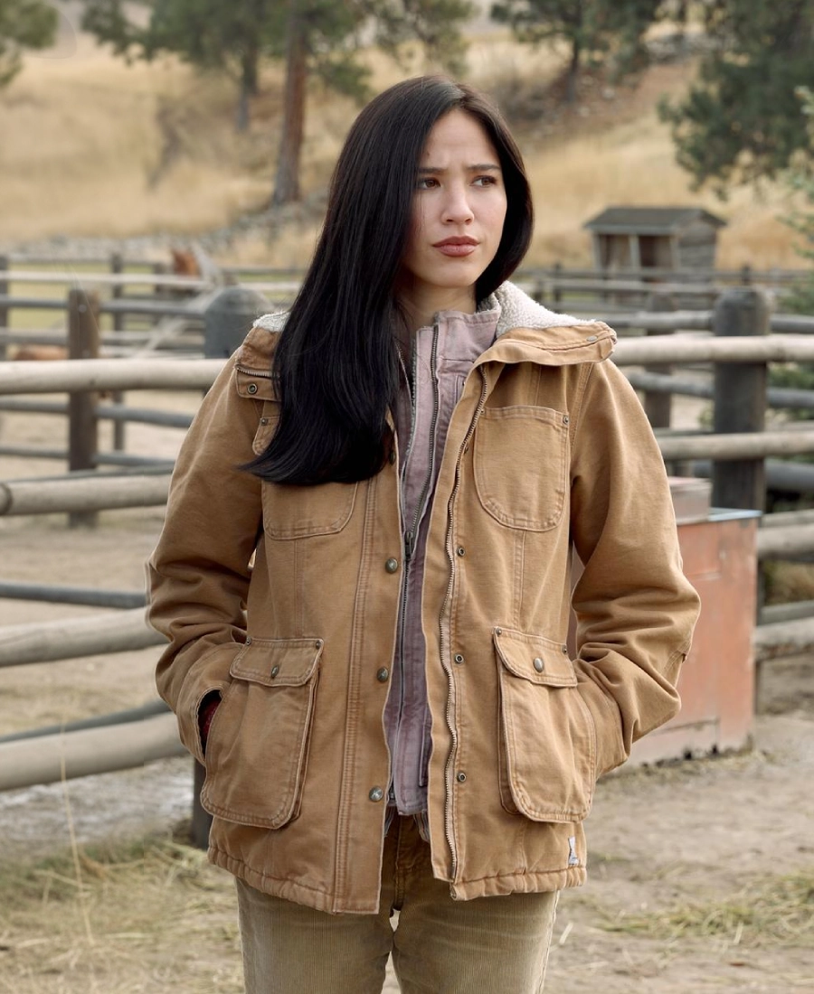 Monica Dutton Yellowstone wearing a brown jacket in an outdoor setting with wooden fences and trees