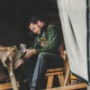 Rip Wheeler sitting at a wooden table in a rustic setting, wearing a green vest.