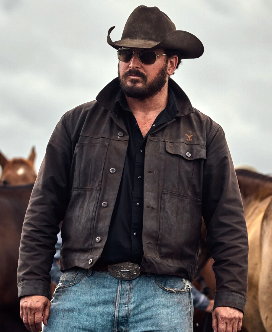 Rip wearing a cowboy hat, sunglasses, and a black cotton jacket with horses in the background