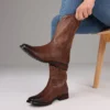 Rip Wheeler Brown cowboy boots with intricate designs worn by a person sitting on a chair.