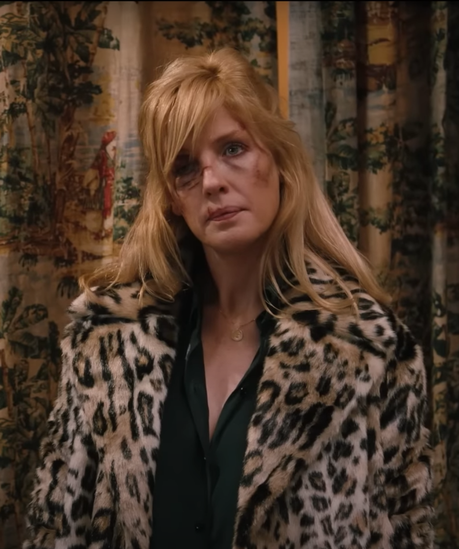 ABeth Dutton wearing a leopard print coat in a room with patterned curtains
