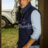John Dutton wearing a navy blue vest, standing outdoors near a vintage truck.