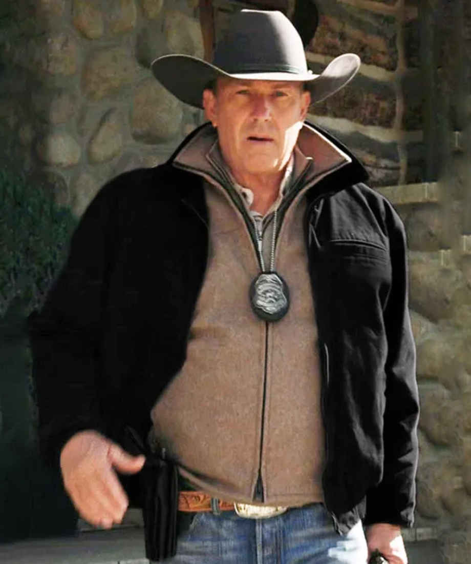 John Dutton wearing a cowboy hat, black jacket, and brown vest against a stone wall.